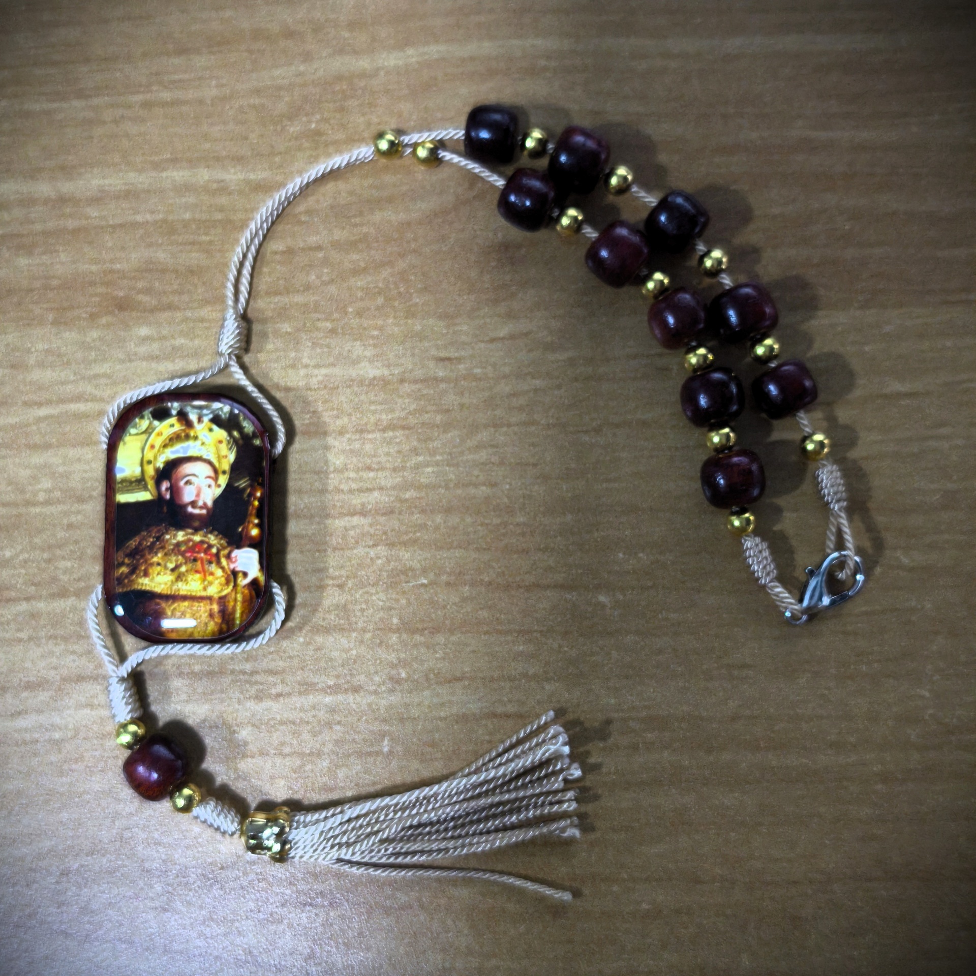 Dezena 3 Rosário com contas de madeira castanha e douradas, cordão bege com franjas e medalha retangular de santo.