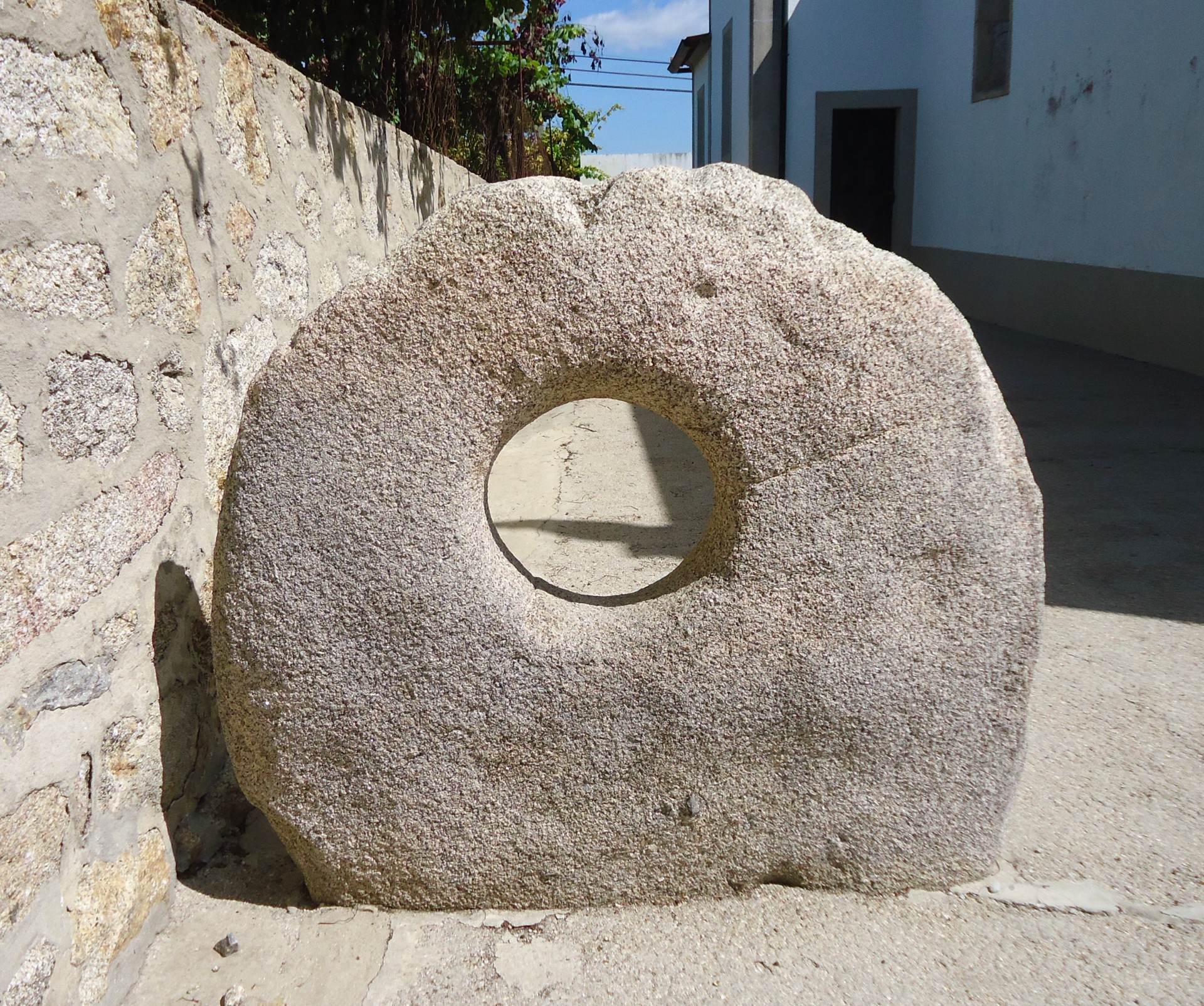 Moinho de pedra redondo com buraco ao centro junto a muro de pedra