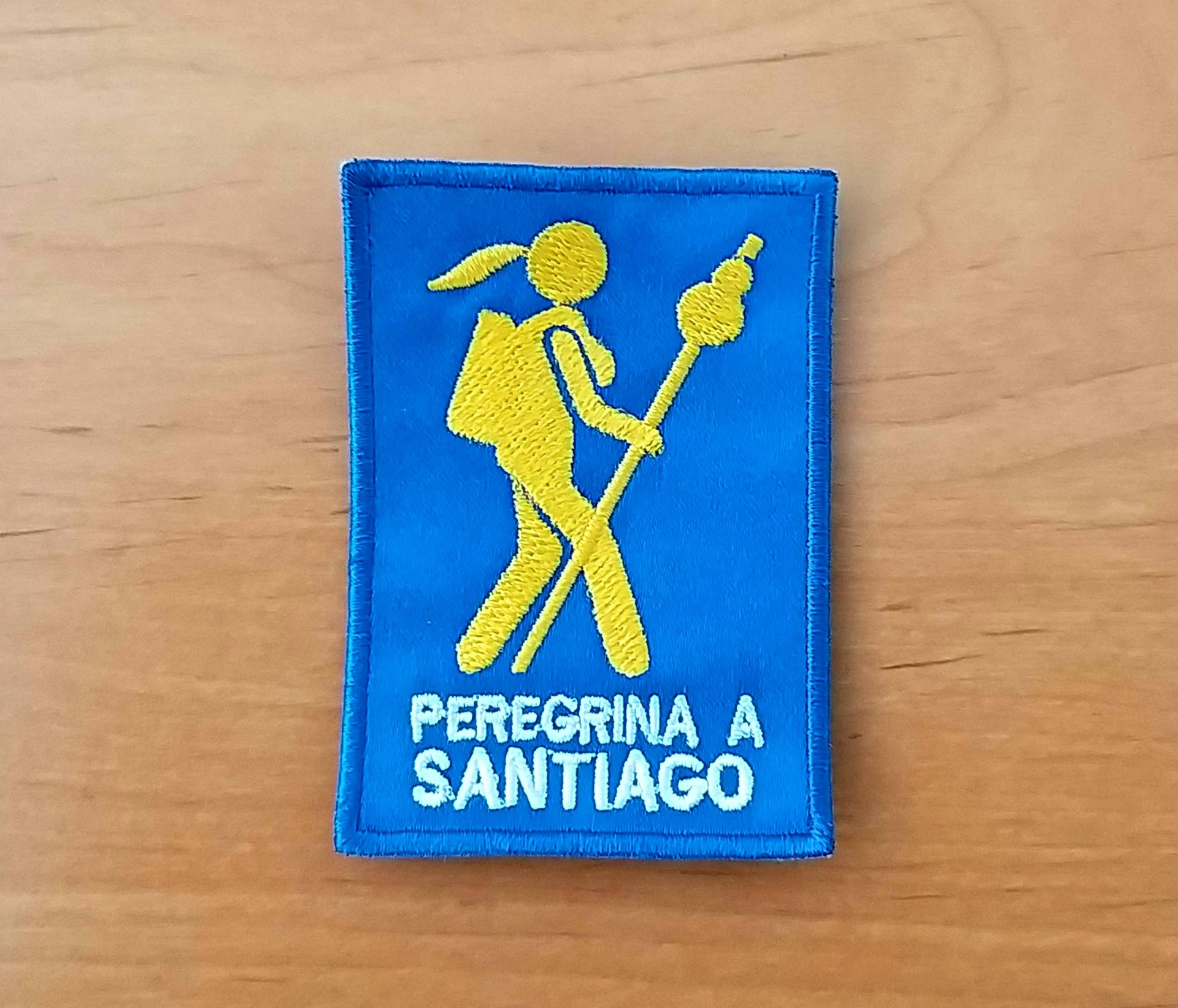 Emblema (Peregrina a Santiago) Emblema bordado azul com figura amarela de peregrino e texto branco PEREGRINA A SANTIAGO
