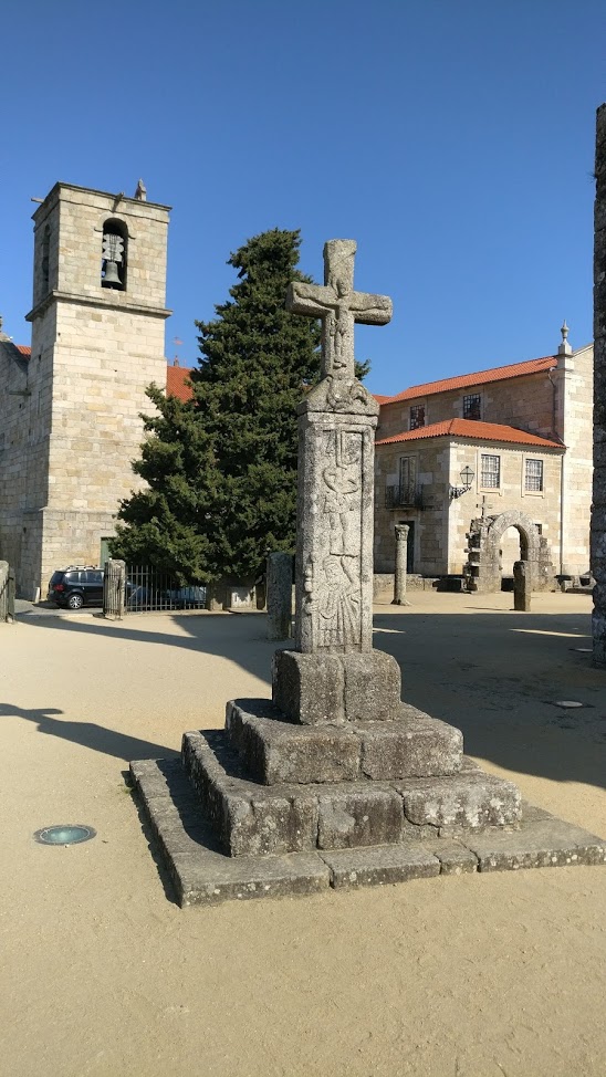 Cruzeiro de pedra cinzenta com esculturas religiosas em praça ao ar livre