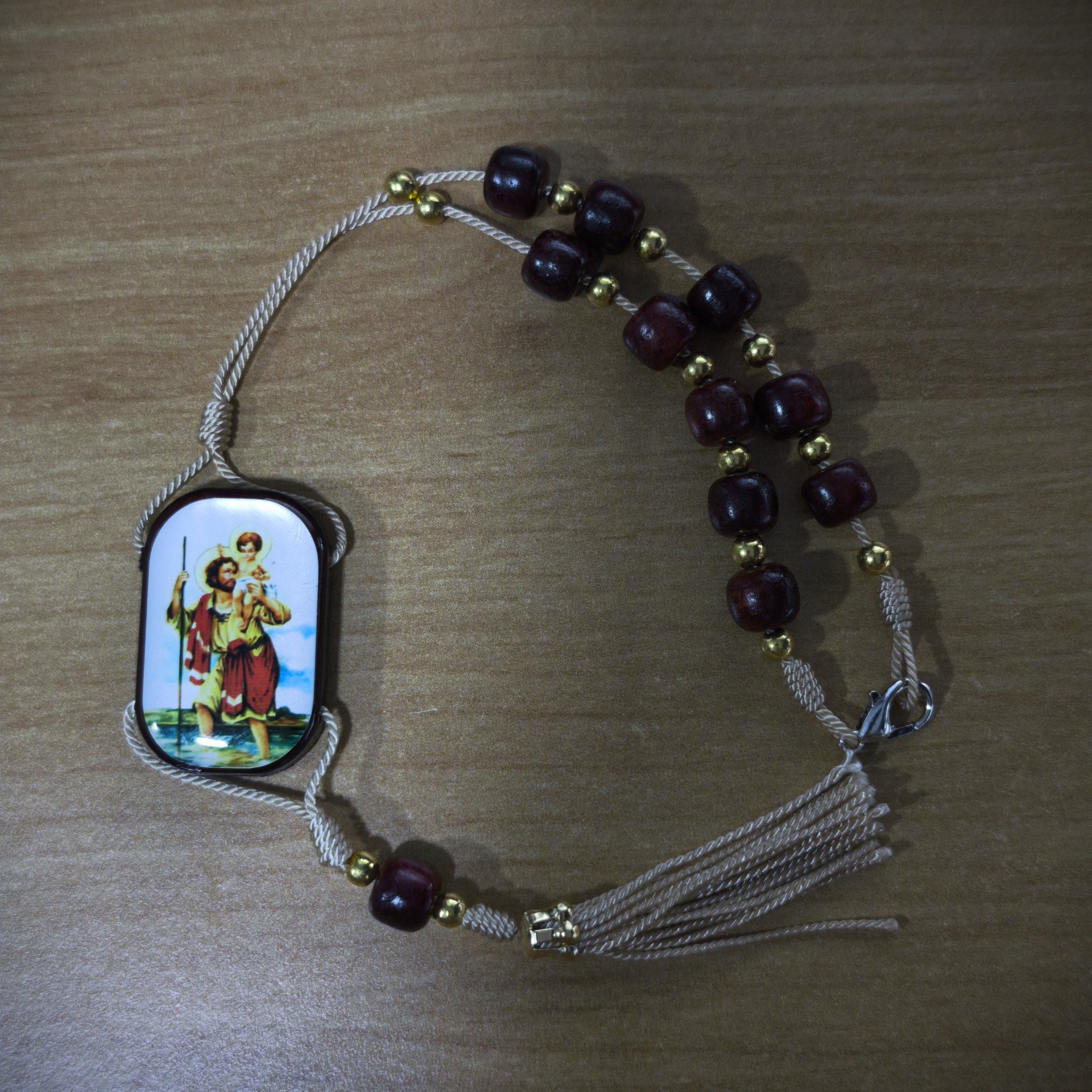 Dezena 3 Pulseira religiosa com contas e medalha de santo em fundo de madeira.