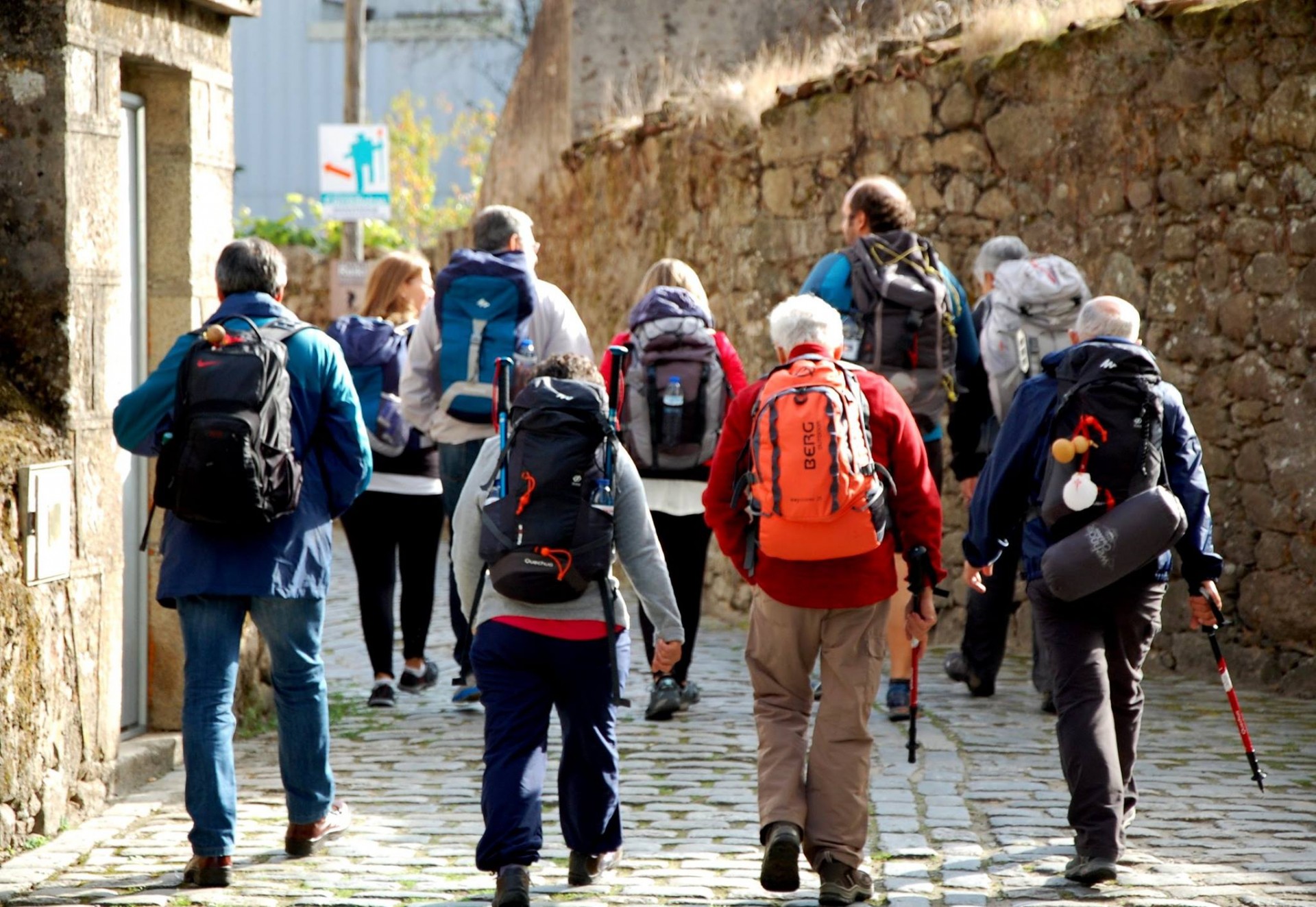 Grupo de pessoas a caminhar numa rua de calçada antiga com mochilas e roupas casuais