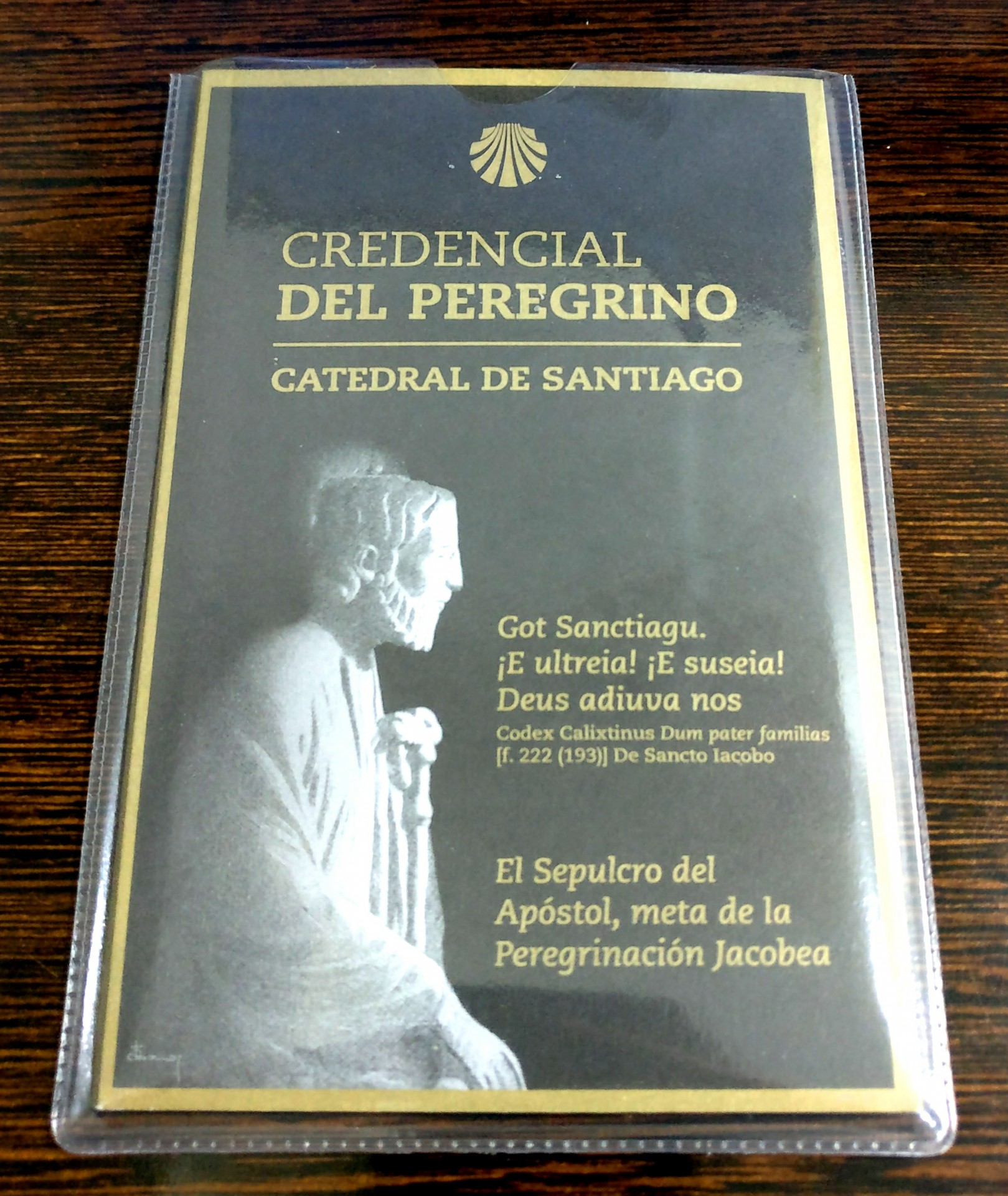 Credencial del Peregrino com capa preta e letras douradas em capa plástica sobre madeira
