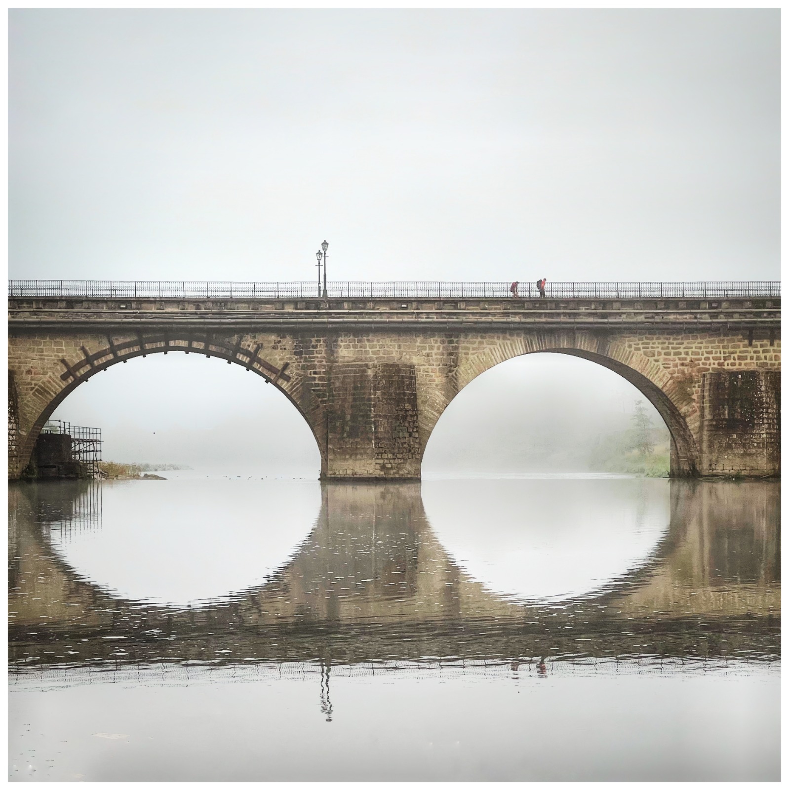 Ponte antiga de pedra com dois arcos grandes sobre um rio calmo