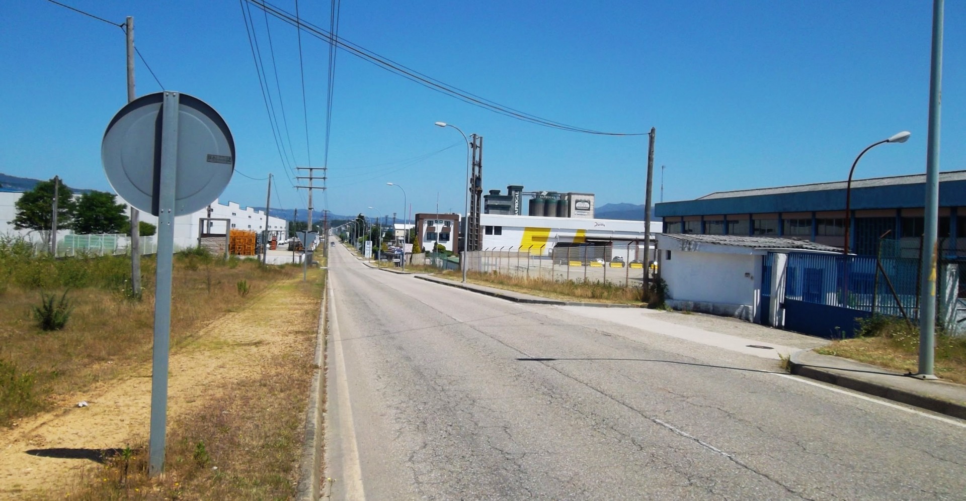Estrada vazia com sinal de trânsito cinzento e edifícios industriais ao fundo