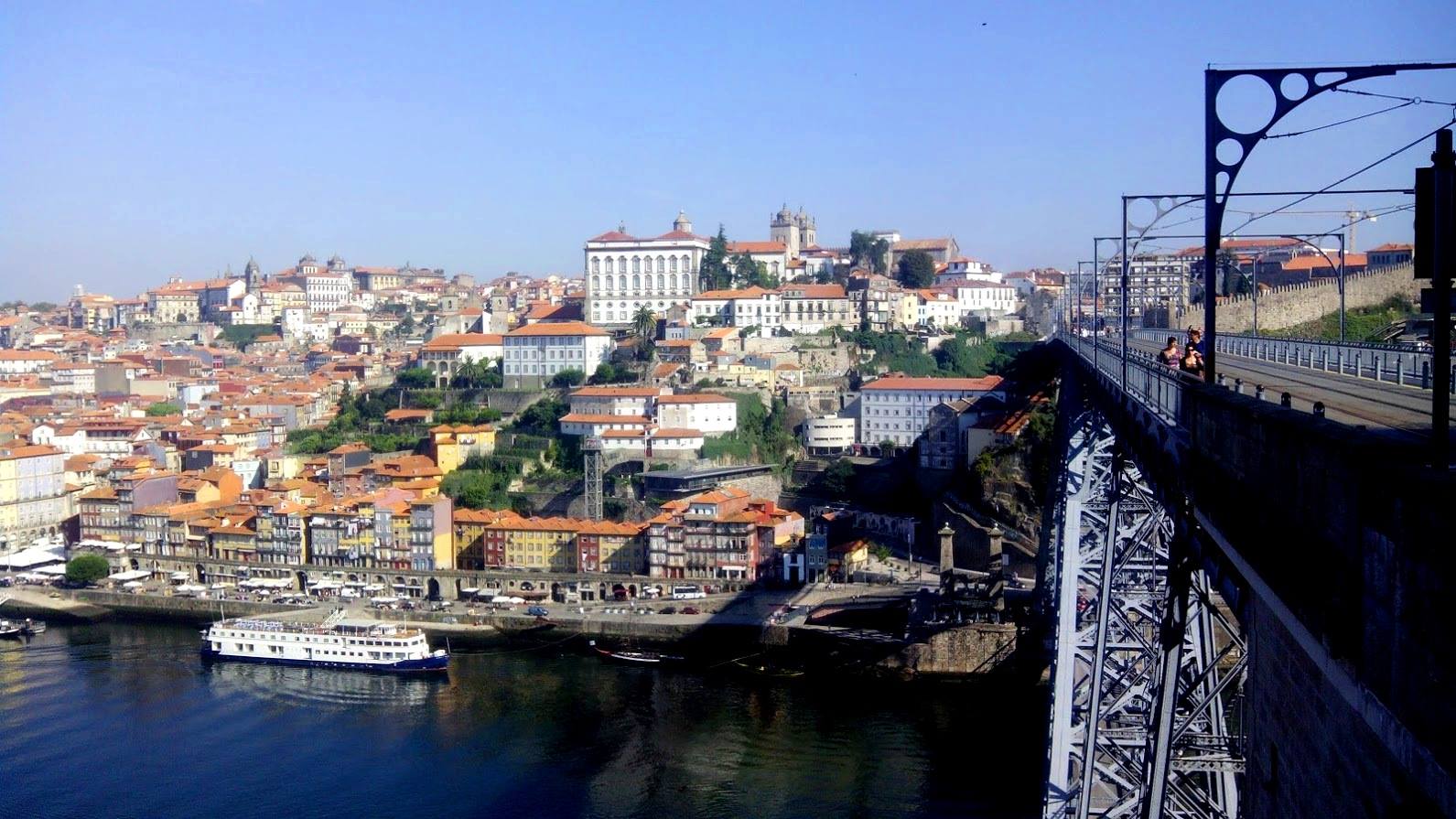 Cidade costeira com ponte metálica azul e barco atracado no rio