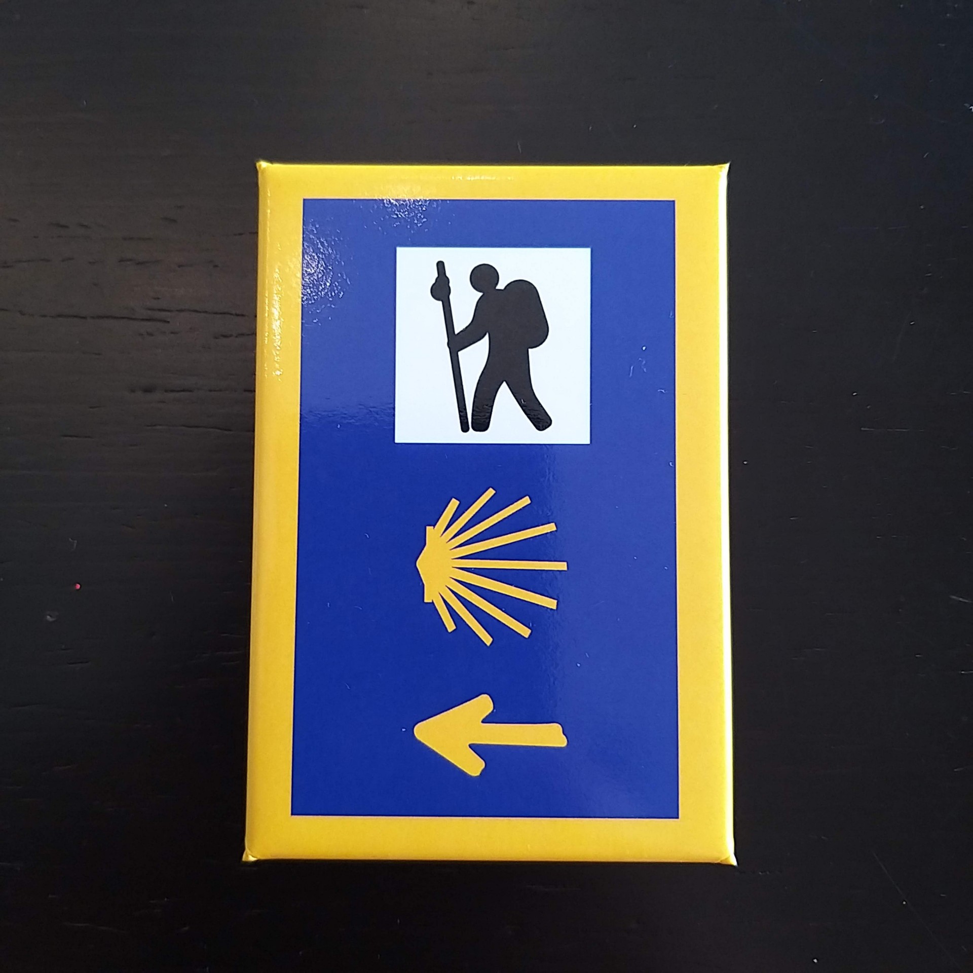 Íman (Sinalização Peregrino) Caixa com símbolo de peregrino, concha e seta amarela sobre fundo azul e amarelo