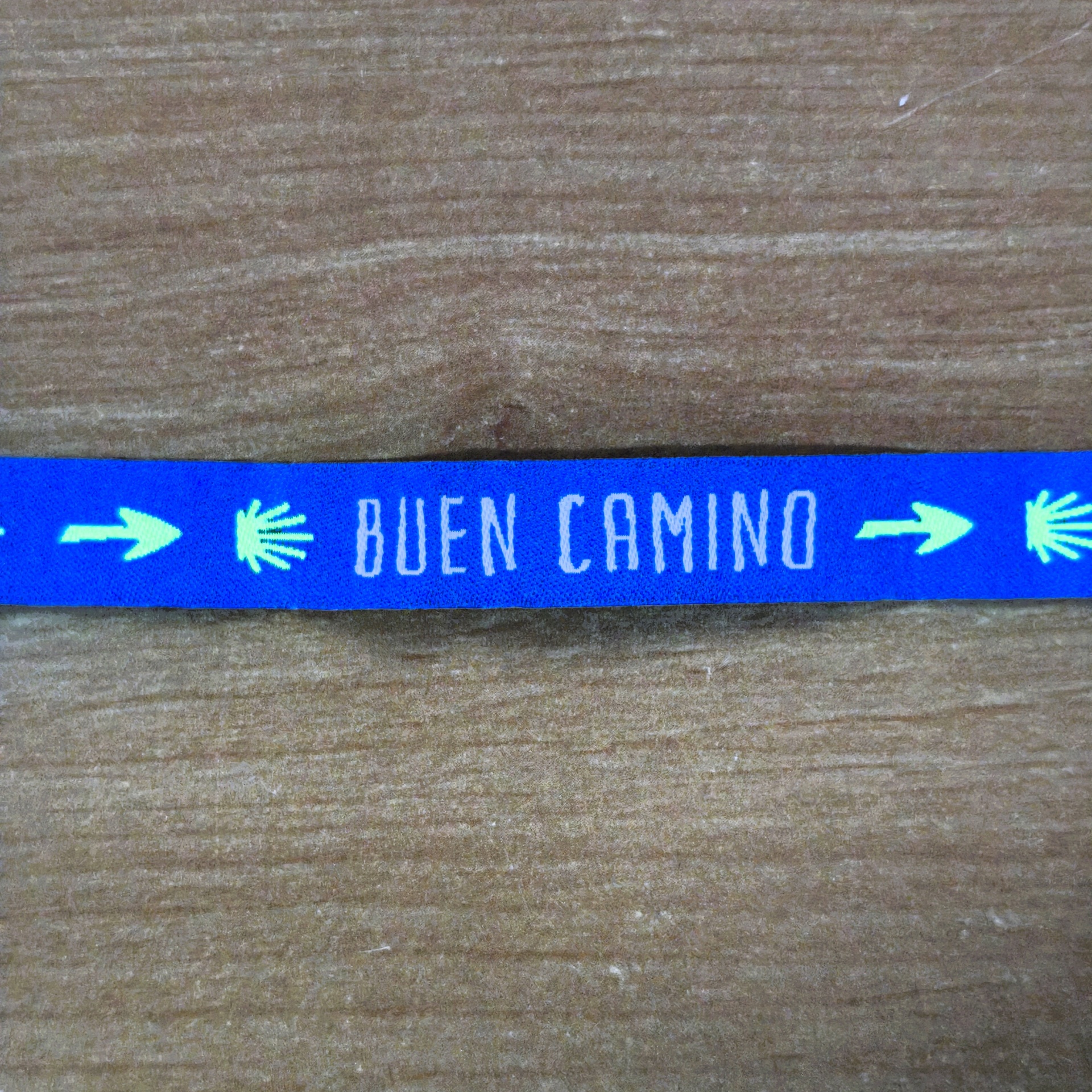Pulseira "Buen Camino" Tira azul com setas amarelas, conchas do mar e texto BUEN CAMINO em branco