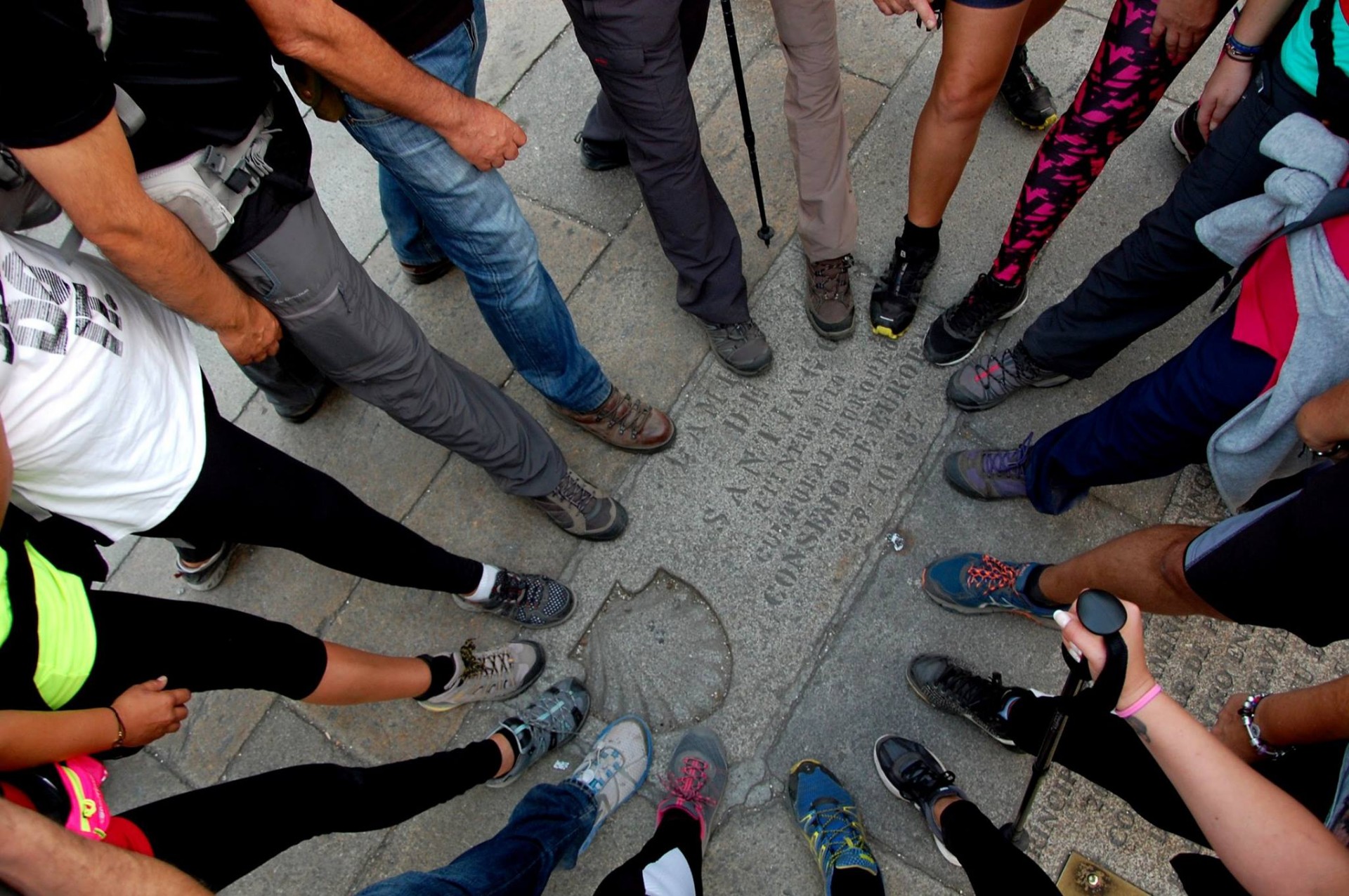 Pessoa em círculo com sapatos desportivos variados sobre chão de pedra com placa gravada.