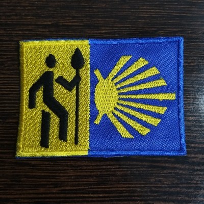 Etiqueta bordada com figura humana, lança e concha em fundo amarelo e azul