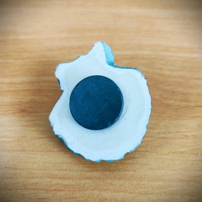 Íman redondo preto numa peça branca irregular sobre madeira clara