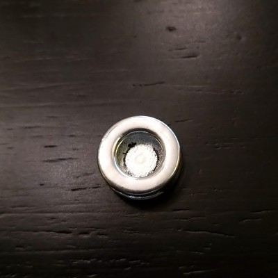 Objeto redondo com borda prateada e centro branco sobre superfície escura