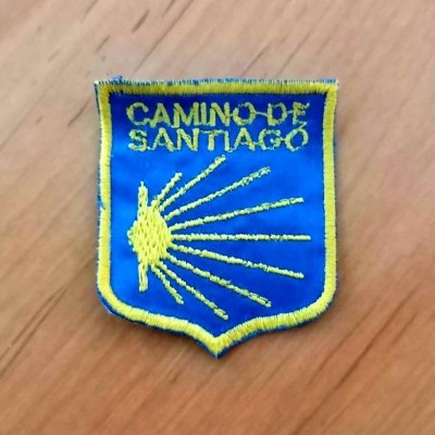 Emblema tecido azul e amarelo com texto Camino de Santiago e concha estilizada