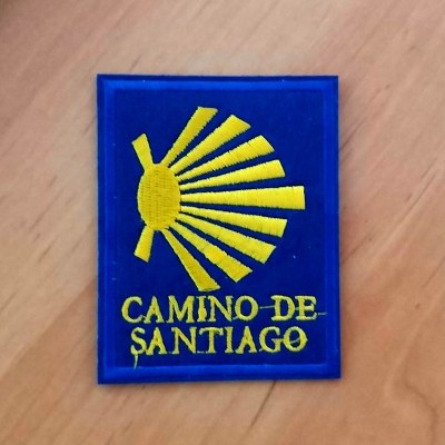 Emblema azul com concha amarela e texto CAMINO DE SANTIAGO