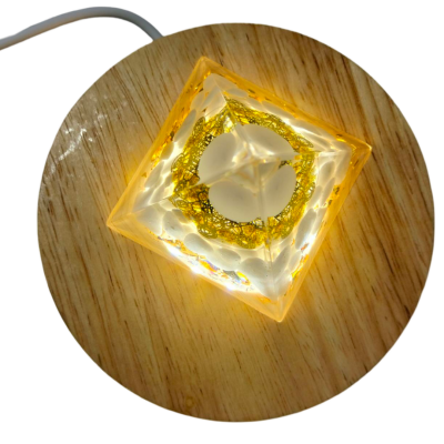 Luz decorativa quadrada translúcida com detalhes dourados, sobre suporte de madeira