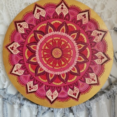Placa decorativa redonda com mandala rosa e dourado em fundo branco com franjas.