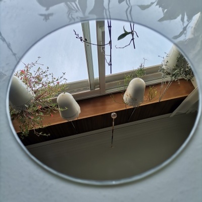 Espelho redondo refletindo janela, plantas e candeeiros brancos