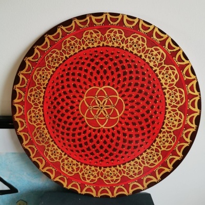 Prato decorativo redondo com padrão geométrico em vermelho, amarelo e preto na parede