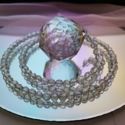 Esfera facetada transparente e colar de contas sobre superfície espelhada