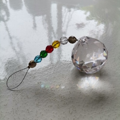 Pingente decorativo com esfera facetada e cristais coloridos sobre superfície branca