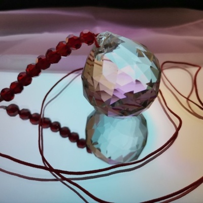 Pendente de cristal prismático com contas vermelhas sobre superfície espelhada