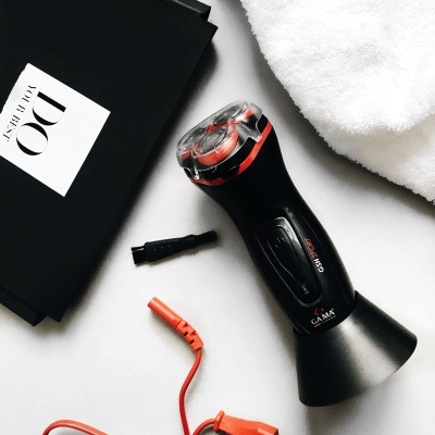 Barbeador elétrico preto com cabo laranja ao lado de uma toalha branca e caixa preta