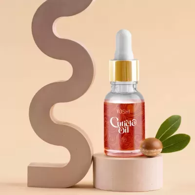 Frasco de óleo para cutículas Yoshi com conta-gotas, noz e folhas verdes sobre pedestal creme e fundo bege abstrato