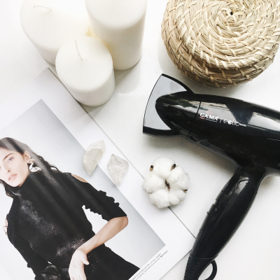 Secador de cabelo preto, velas brancas, recipiente de palha, flor de algodão e página de revista com mulher de vestido preto.