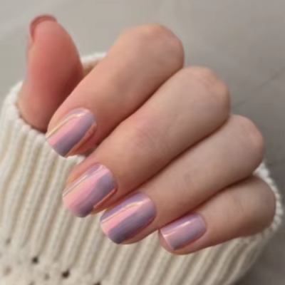 Unhas manicadas com verniz lilás claro e reflexos rosados em mão com camisola de malha.