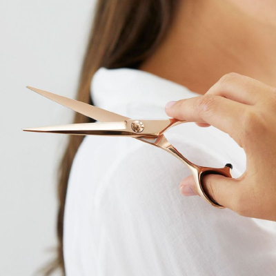 Tesoura dourada rosada segura com mão sobre camisa branca