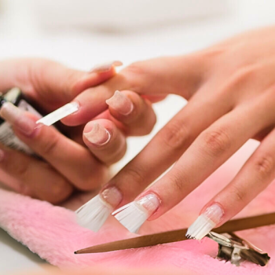 Mãos femininas com unhas postiças aplicadas e escova branca para manicure sobre tecido cor-de-rosa
