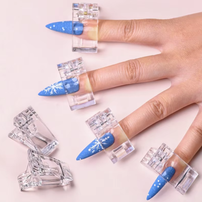 unhas azuis com decalques de flocos de neve e grampos transparentes numa mão em fundo rosa