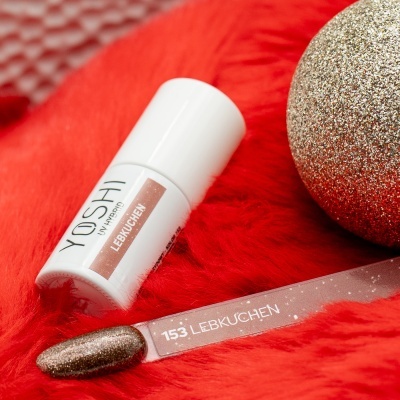Esmalte de unhas branco YOSHI 153 LEBKUCHEN numa superfície vermelha felpuda com bola decorativa dourada.