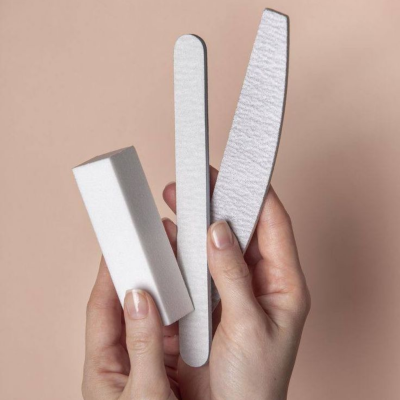 Mãos segurando três lixas de unha brancas em fundo bege