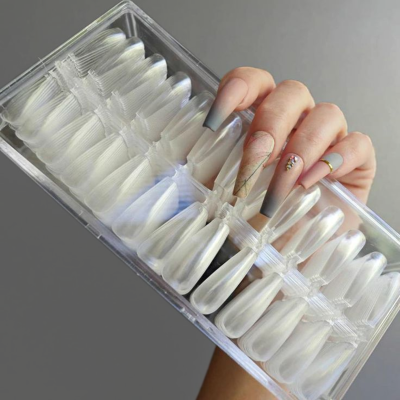 Caixa transparente com unhas postiças brancas peroladas e mão com unhas decoradas