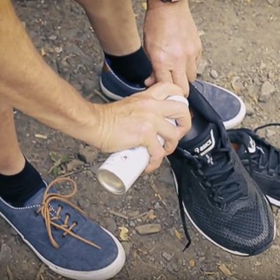 Pessoa a usar sapatos azuis e outra a calçar sapatilhas pretas no chão de terra.