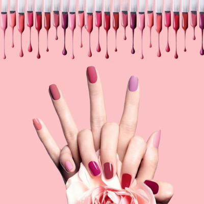 Mãos femininas com unhas pintadas em vários tons de rosa e vermelho segurando uma flor rosa clara sobre fundo rosa.