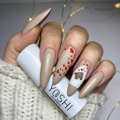 Unhas compridas decoradas em bege e branco com corações e urso, segurando frasco branco YOSHI UV HYBRID