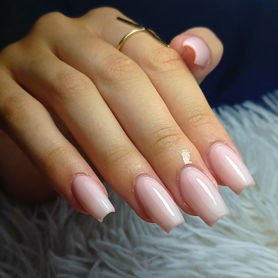 Unhas compridas rosa claro brilhante com anel dourado numa mão feminina