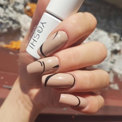 Mão feminina a segurar esmalte de unhas branco YOSHI com unhas nude decoradas com linhas pretas curvas