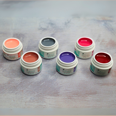 Seis frascos abertos de gel para unhas em várias cores sobre uma superfície de madeira clara