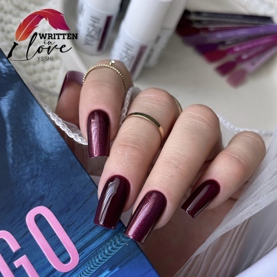 Unhas pintadas em verniz vermelho vinho metálico com anéis delicados e frascos de esmalte YASHI