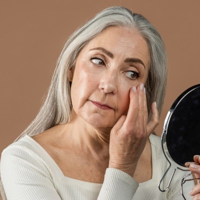 Mulher de cabelos grisalhos a olhar para o espelho de mão redondo