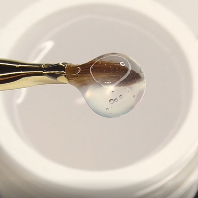 Pincel segurando uma gota viscosa transparente com bolhas sobre fundo branco.