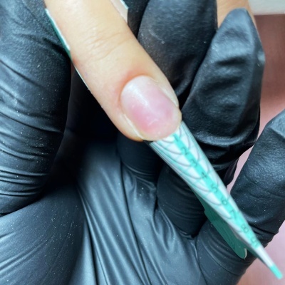 Dedo com extensão de unha e marcações verdes segurado por mão com luva preta