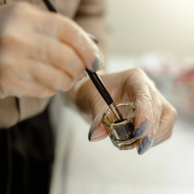 Mãos com luvas segurando copo de vidro e mexendo líquido escuro