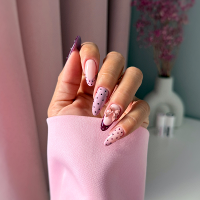 Unhas postiças decoradas com padrões de bolinhas e flor 3D cor-de-rosa, usando casaco rosa claro.