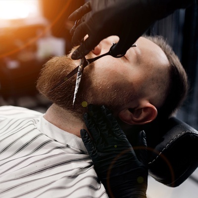 Homem a cortar a barba com tesoura em barbearia