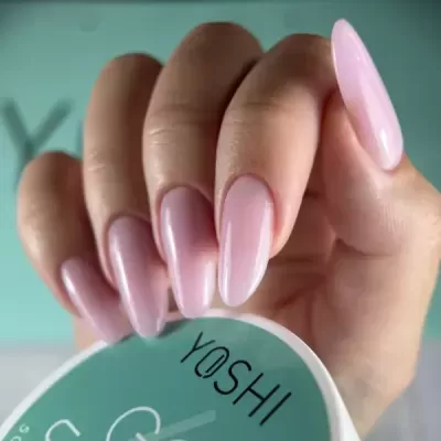 Mãos com unhas rosa claro segurando recipiente YOSHI