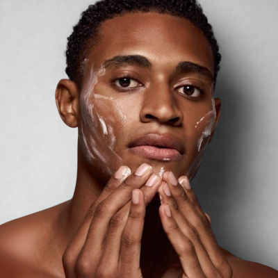 Homem aplicando creme hidratante no rosto com fundo cinzento